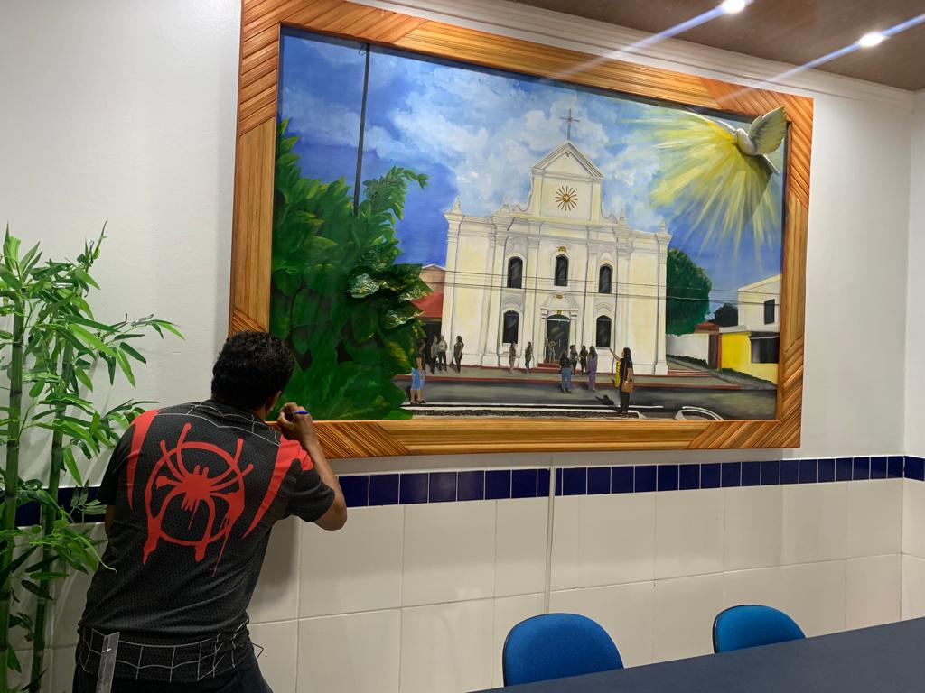 Miguel Barbosa Soares assina um quadro grande de uma igreja branca, já instalado numa parede de azulejos.