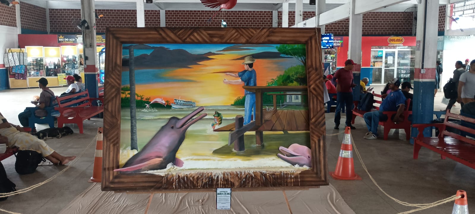 O quadro Botos ao pôr do sol exposto num salão movimentado, com a base que imita a margem do rio.